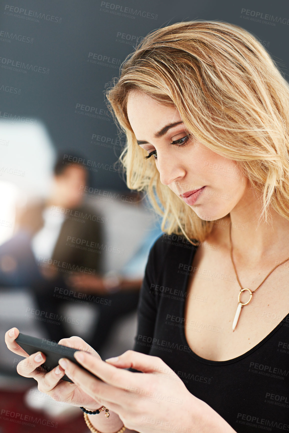 Buy stock photo Shot of a young businesswoman using her cellphone while standing in the office