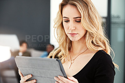 Buy stock photo Shot of a young businesswoman using her tablet while standing in the office