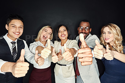 Buy stock photo Portrait of a group of businesspeople showing thumbs up against a dark background