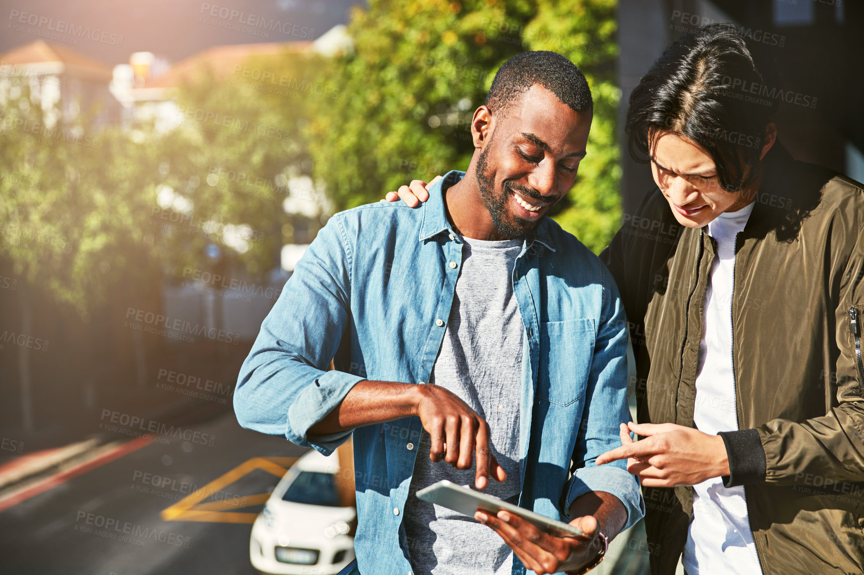 Buy stock photo Shot of two young colleagues looking at a tablet together while standing on a balcony outside their office