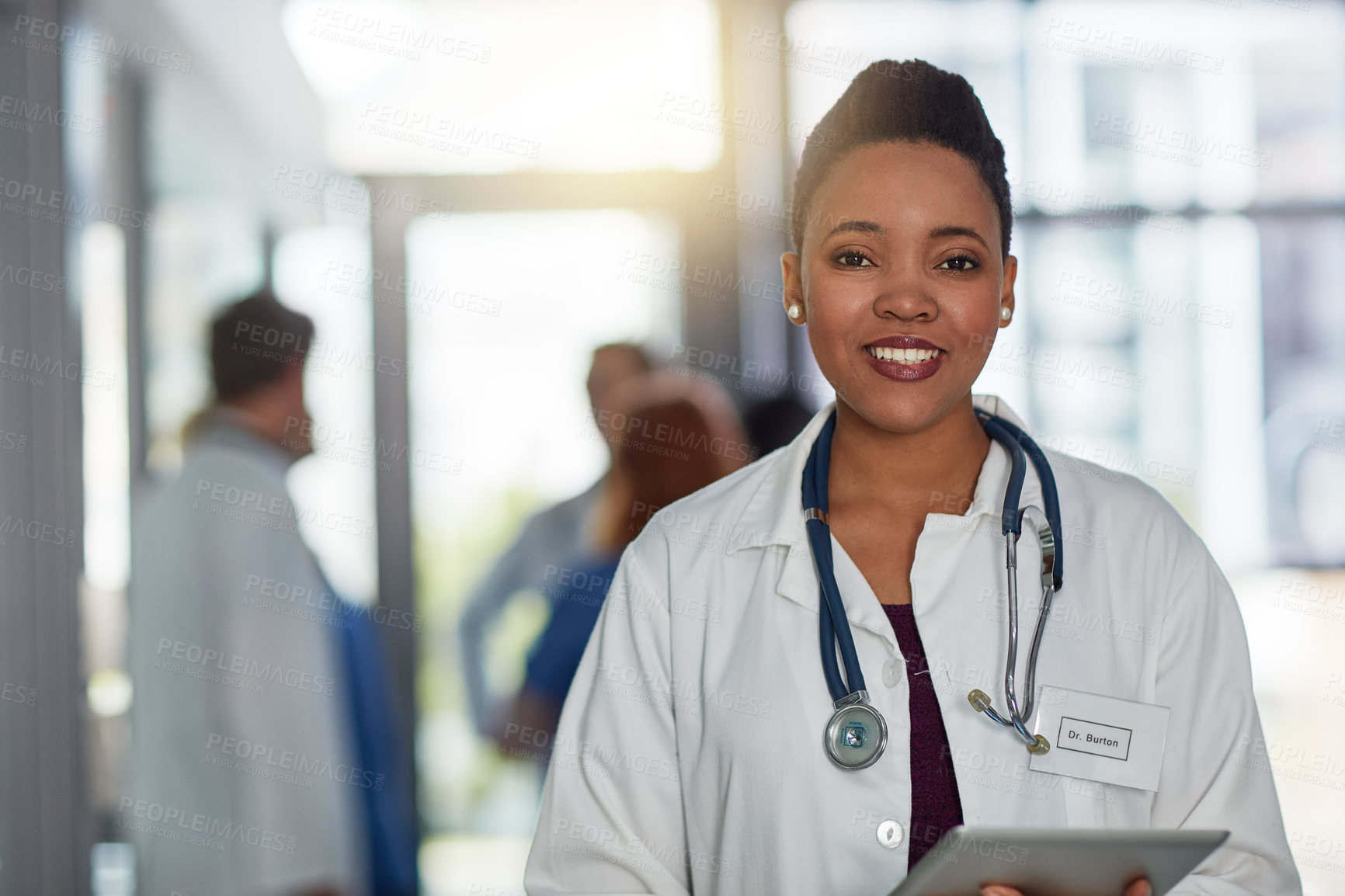 Buy stock photo Portrait of a young female doctor standing in a hospital with her colleagues in the background