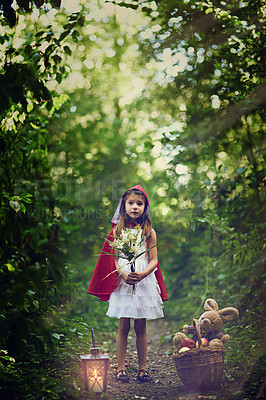 Buy stock photo Shot of a little girl dressed in a red cape holding some flowers in the woods