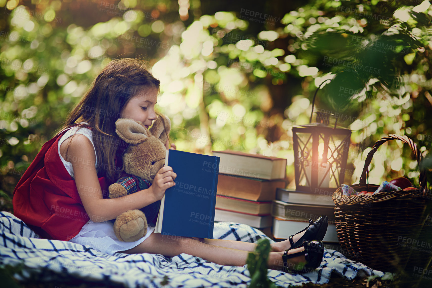 Buy stock photo Picnic, girl and child with book, reading and smile for red cloak, nature and forest for fun and relax. Woods, outdoor and kid with teddy bear, basket and blanket in park, trees and happy youth