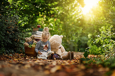 Buy stock photo Shot of a little girl reading to her toys while out in the woods