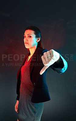 Buy stock photo Portrait of an unimpressed businesswoman giving a thumbs down against a dark background