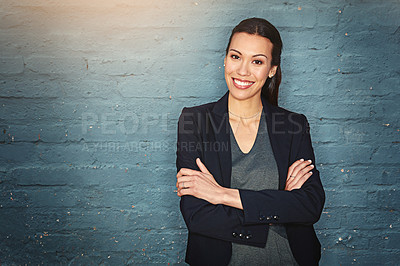 Buy stock photo Portrait of a confident young businesswoman posing against a brick wall with her arms crossed