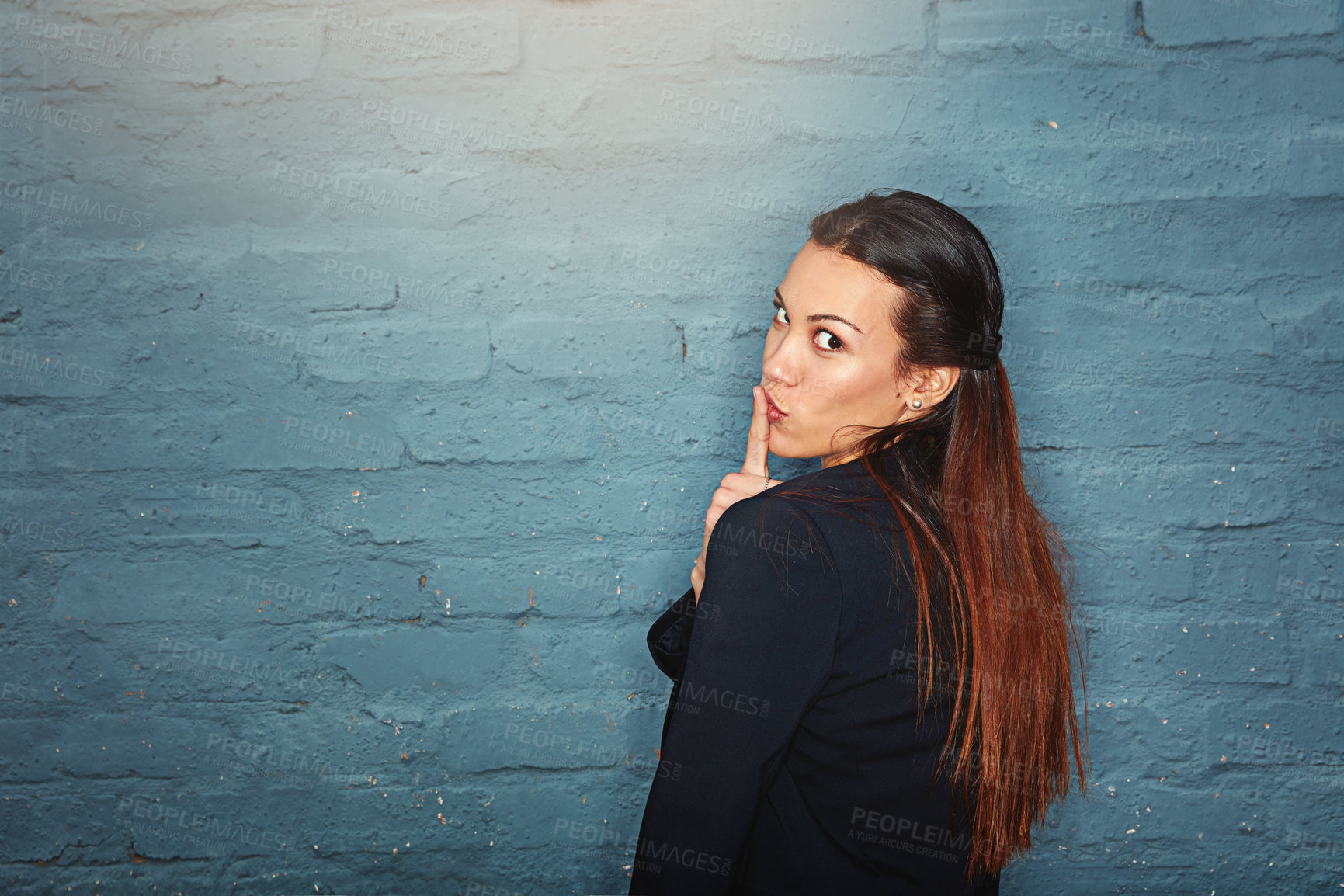 Buy stock photo Portrait of a young businesswoman holding a finger to her lips while looking over her shoulder