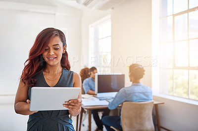 Buy stock photo Shot of a young entrepreneur using a digital tablet at work with her team in the background