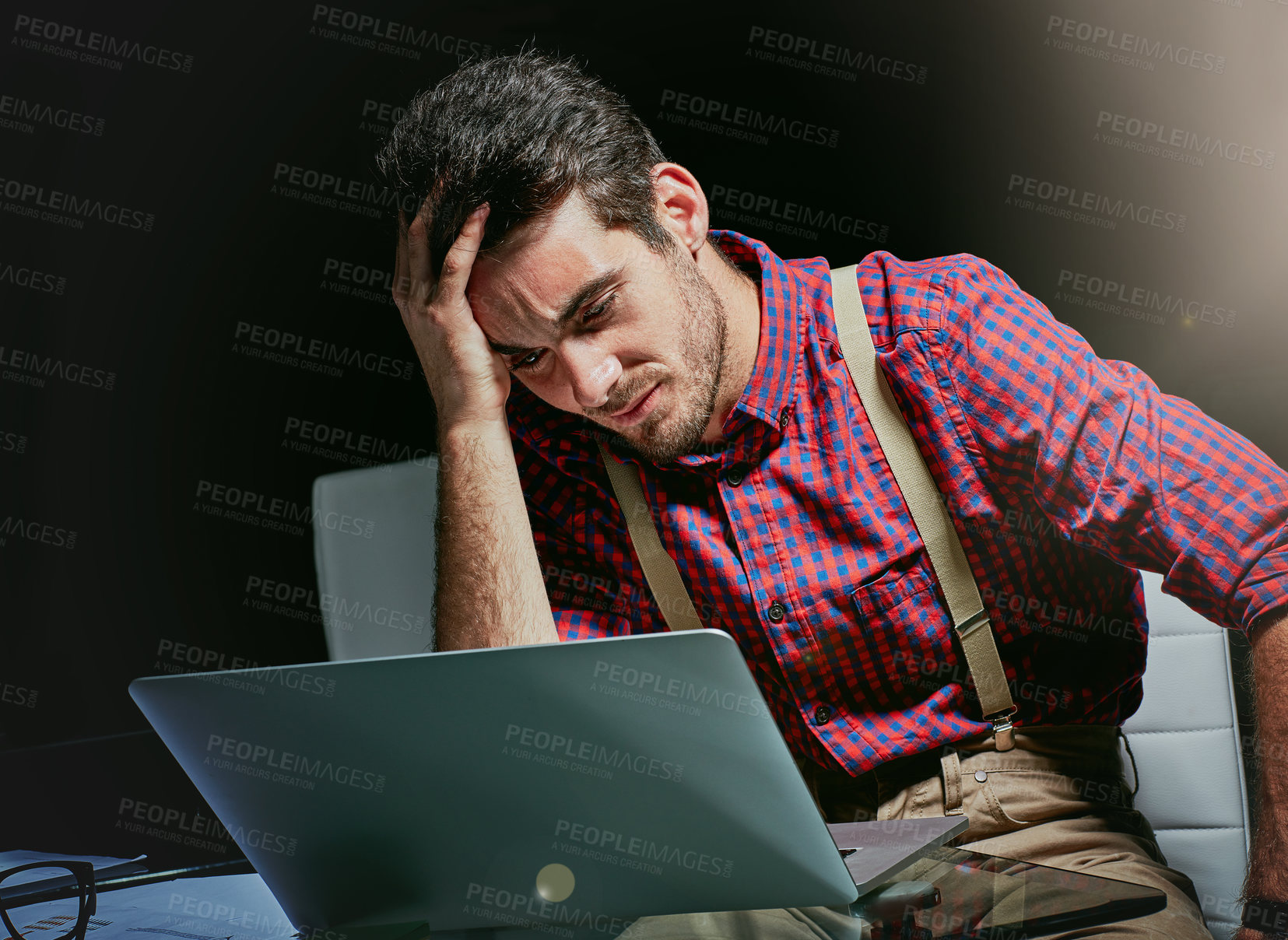 Buy stock photo Shot of a frustrated young designer looking stressed while working on his laptop