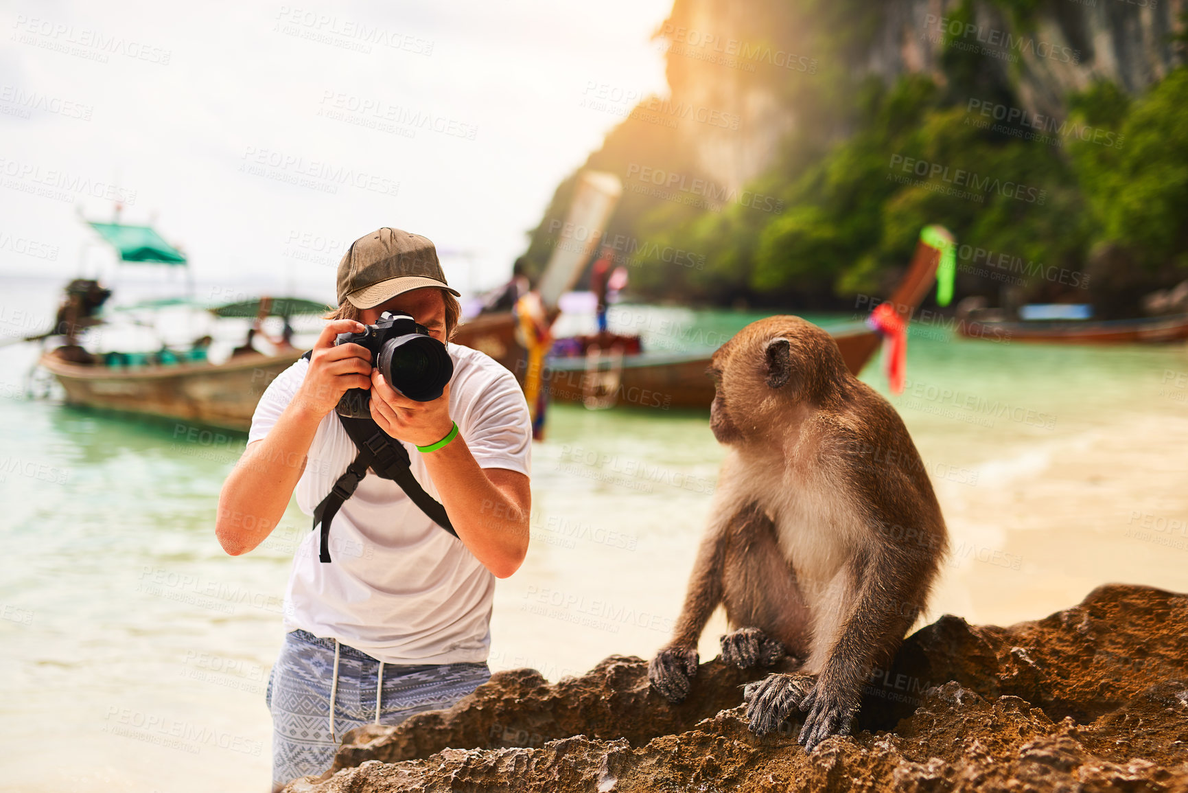 Buy stock photo Shot of a young tourist taking a picture of a monkey while exploring a tropical beach