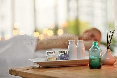 Buy stock photo Cropped shot of various pampering essentials in a spa with a young woman in the background