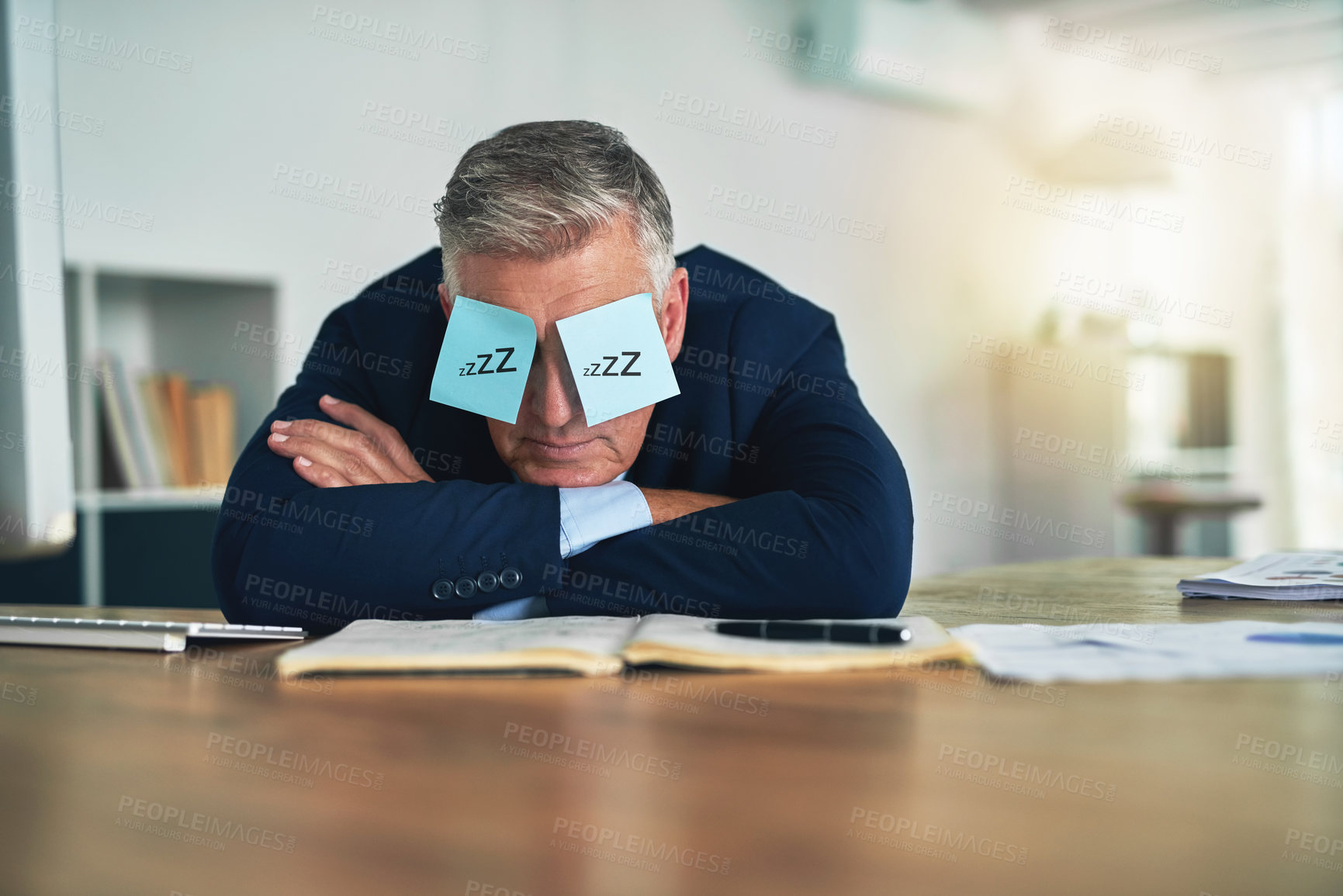Buy stock photo Shot of a tired businessman napping at his desk with adhesive notes on his eyes