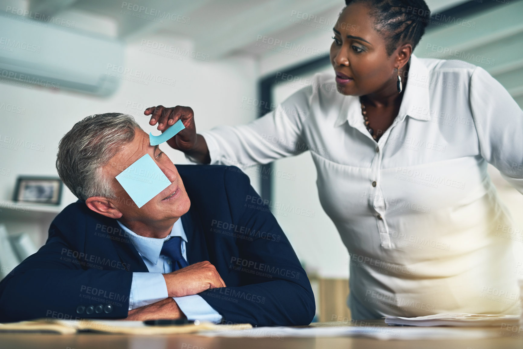 Buy stock photo Shot of a businesswoman removing adhesive notes from her coworker's eyes as he sleeps at his desk