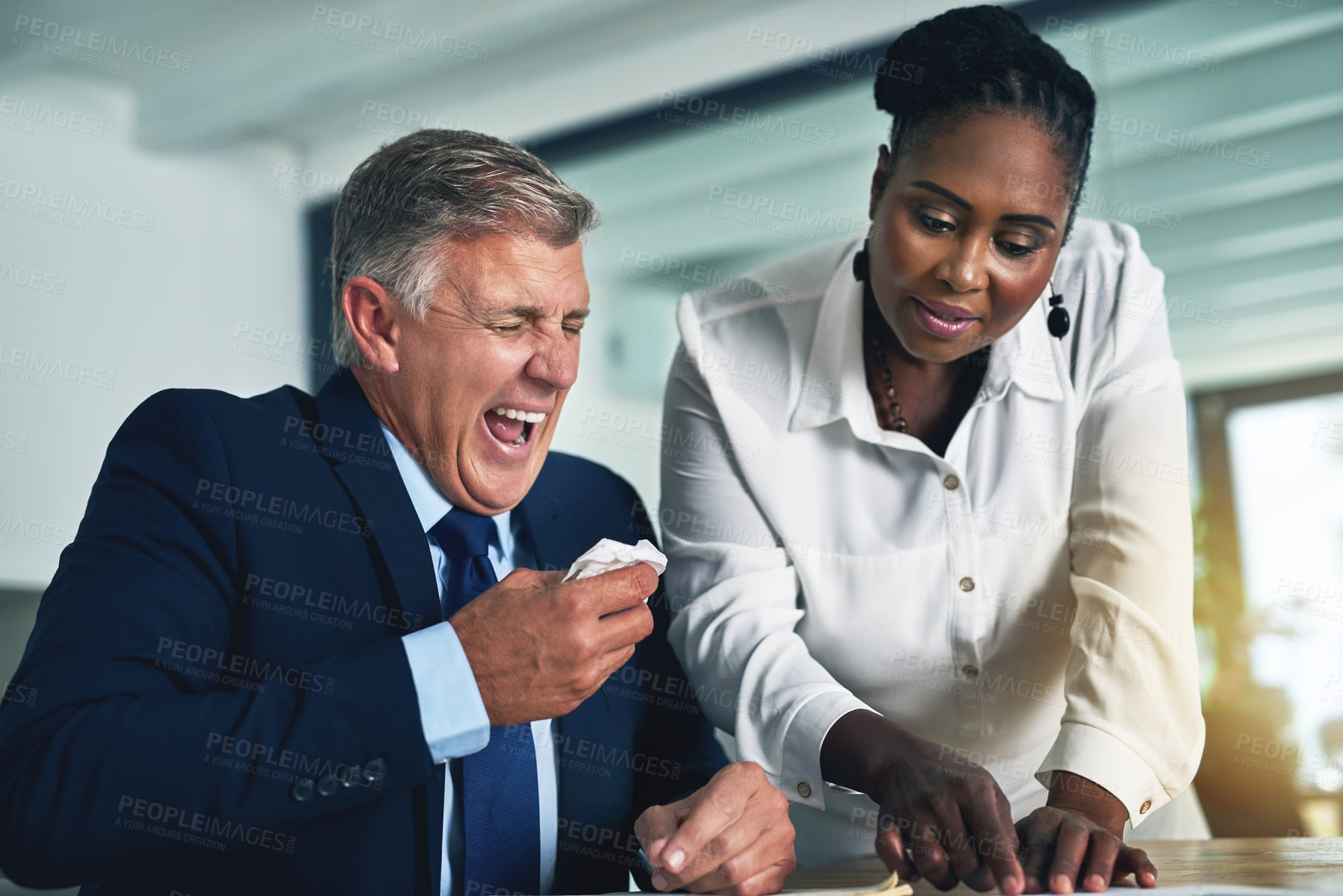 Buy stock photo Shot of a businessman experiencing hayfever while working at his desk with a colleague