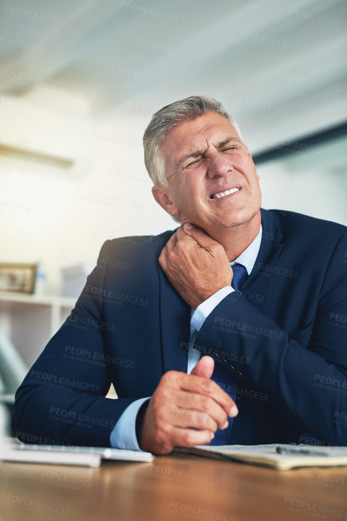 Buy stock photo Shot of a wincing businessman holding his stiff neck while sitting at a desk in the office