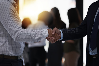 Buy stock photo Shot of two silhouetted businesspeople shaking hands in front of a window in the office