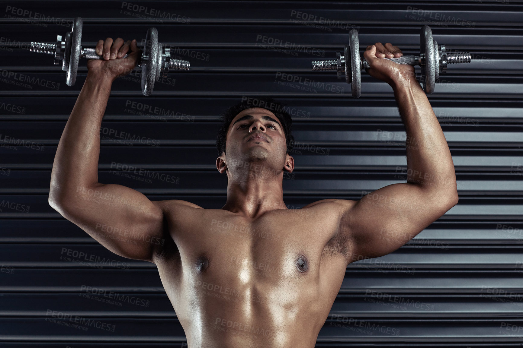 Buy stock photo Cropped shot of a handsome young man working out with dumbbells