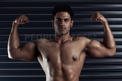 Buy stock photo Cropped portrait of an athletic young man flexing his biceps against a dark background