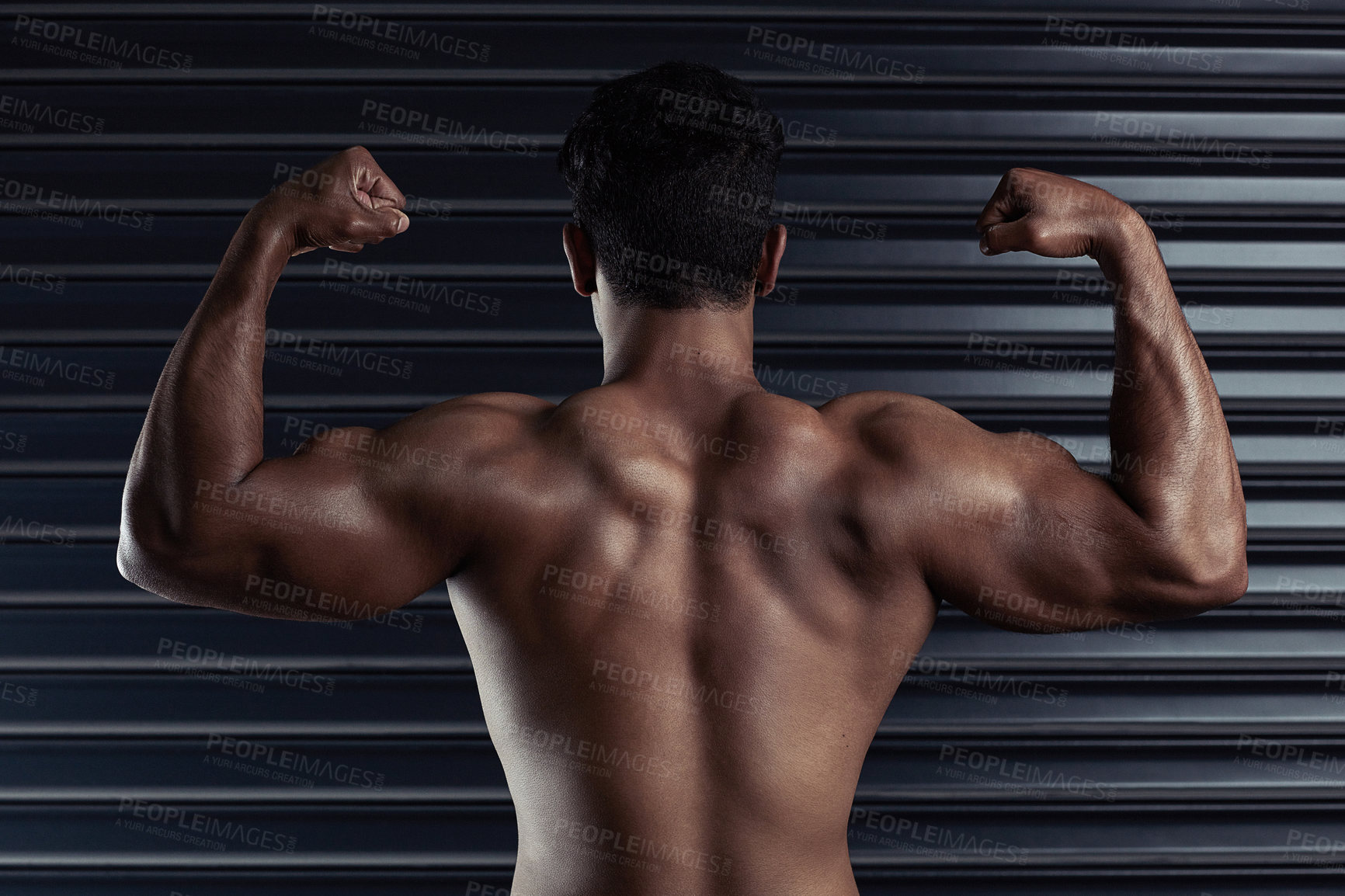Buy stock photo Rearview shot of an athletic young man flexing his biceps against a dark background