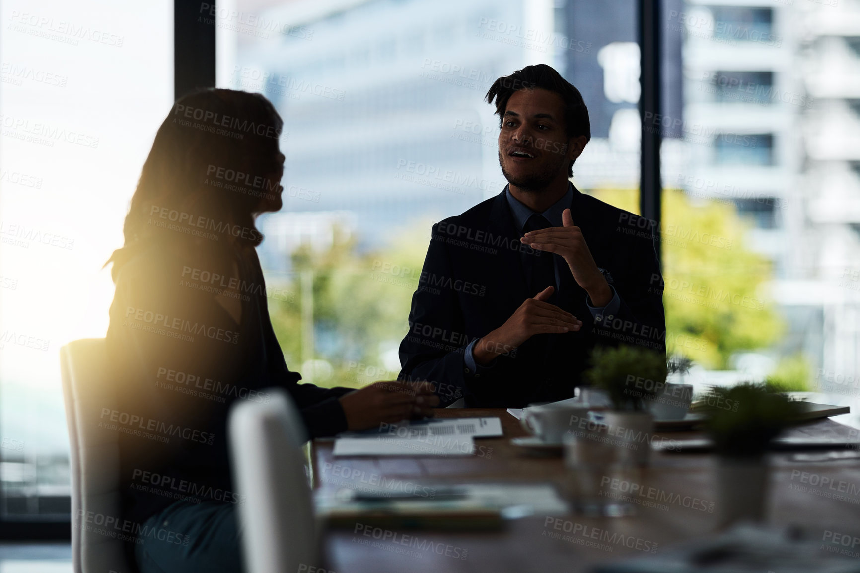 Buy stock photo Shot of two silhouetted businesspeople having a meeting in the boardroom