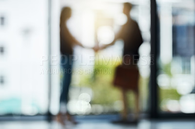 Buy stock photo Defocussed shot of two silhouetted businesspeople shaking hands in front of a window in the office