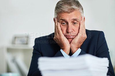 Buy stock photo Shot of a mature businessman looking at paperwork and feeling overwhelmed