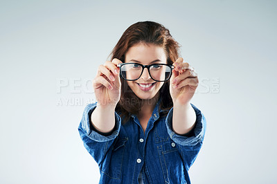 Buy stock photo Studio portrait of a young woman holding a pair of spectacles against a grey background