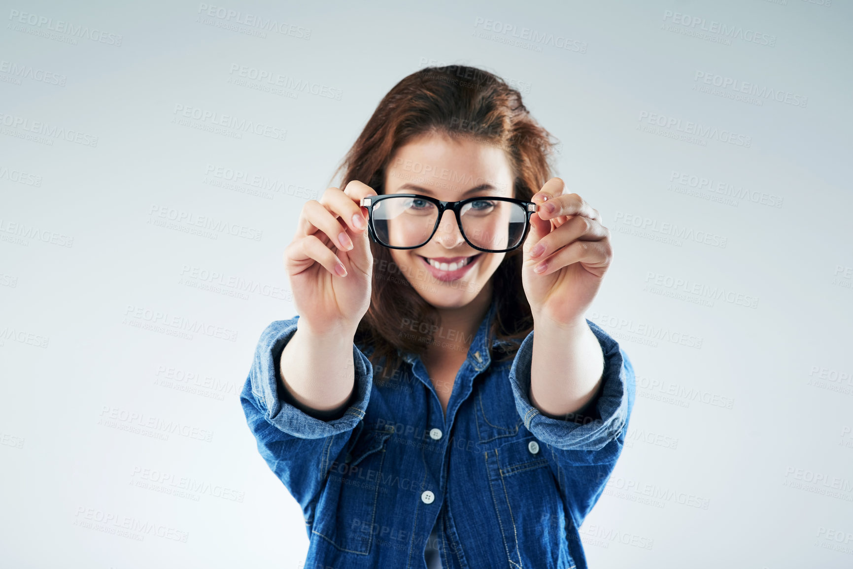 Buy stock photo Studio portrait of a young woman holding a pair of spectacles against a grey background