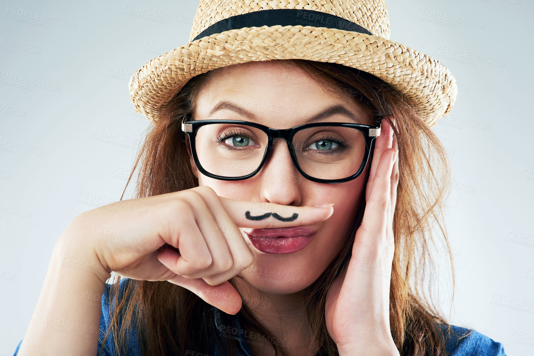 Buy stock photo Studio portrait of a young woman holding her finger under her nose with a moustache drawn on it