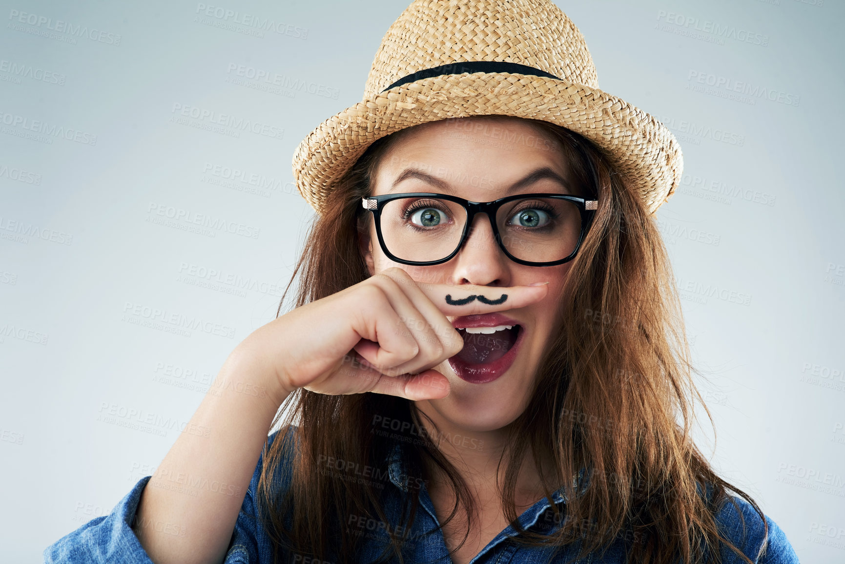Buy stock photo Studio portrait of a young woman holding her finger under her nose with a moustache drawn on it