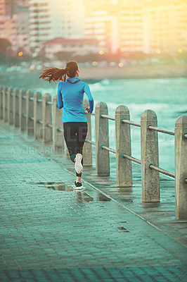 Buy stock photo Shot of a sporty young woman out running on the promenade