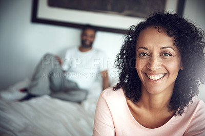 Buy stock photo Portrait of a happy mature woman sitting on the edge of the bed with her husband in the background
