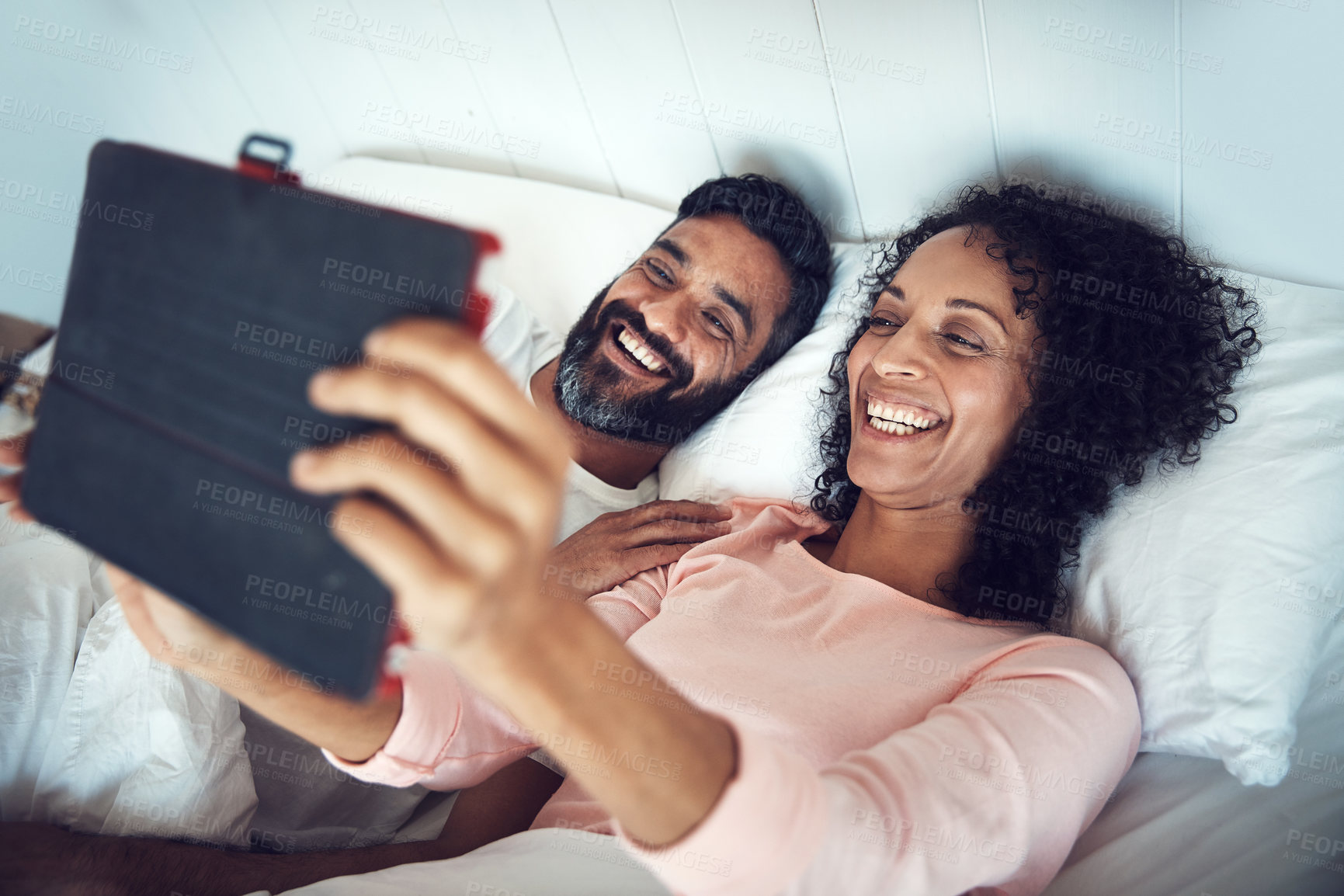 Buy stock photo Shot of a mature couple using a digital tablet while relaxing together in bed