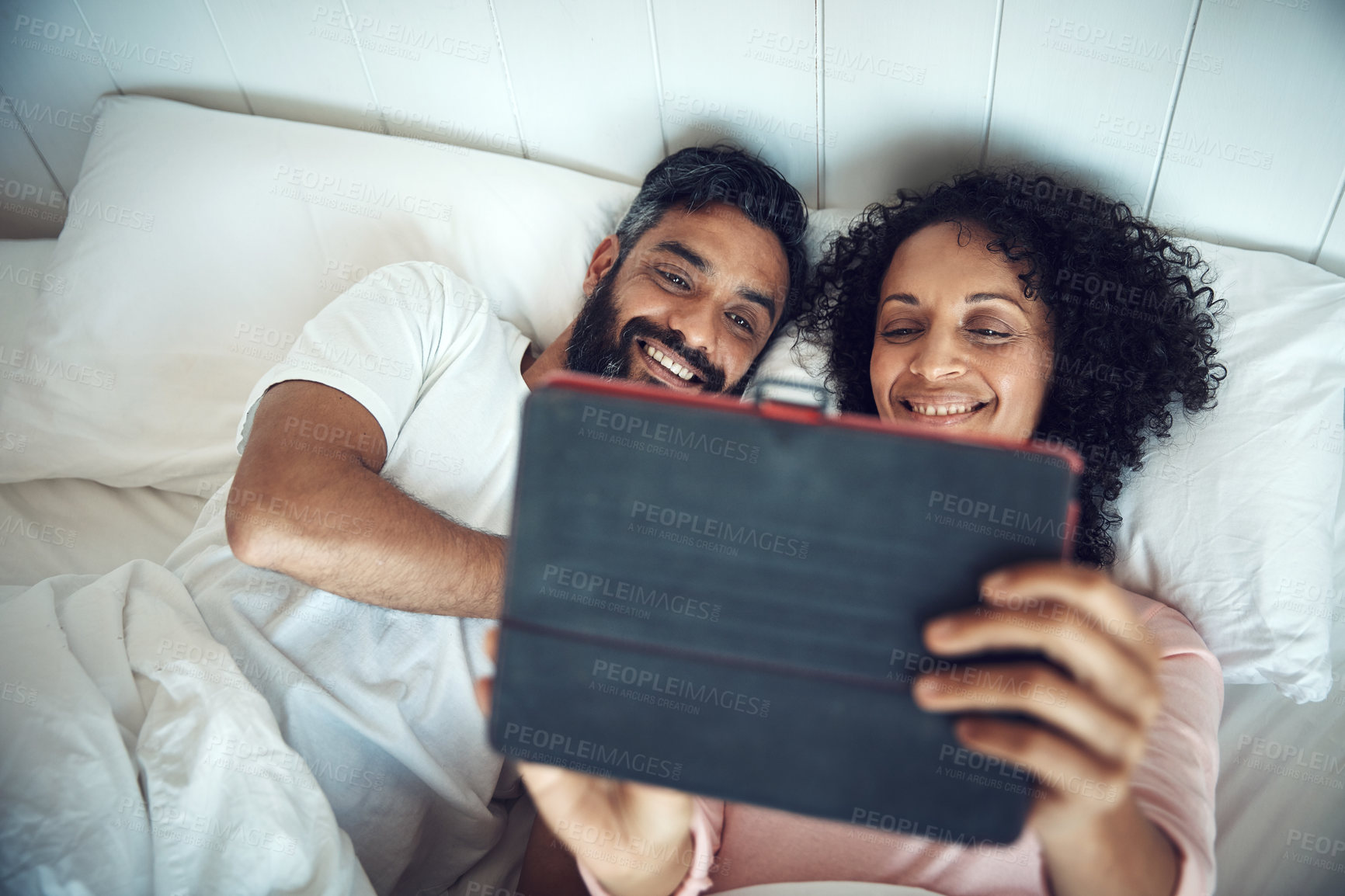 Buy stock photo Shot of a mature couple using a digital tablet while relaxing together in bed