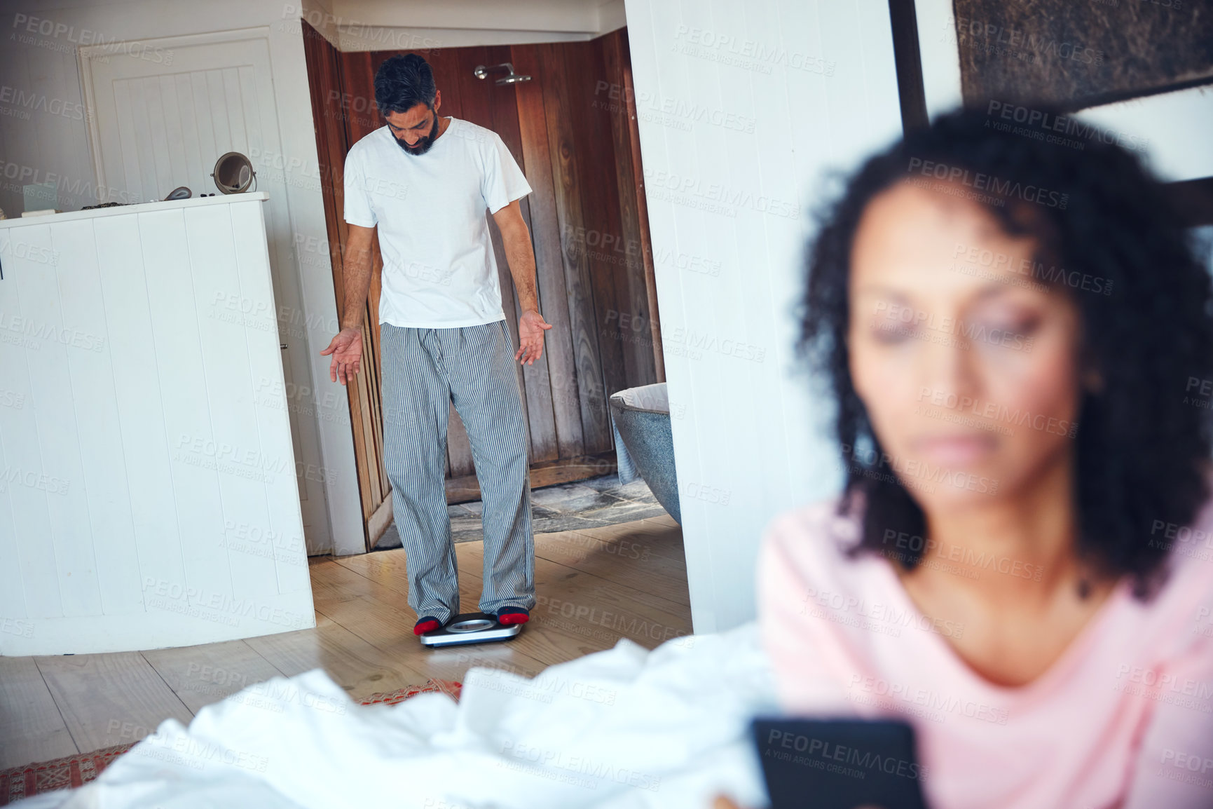 Buy stock photo Shot of a mature man weighing himself on a scale with his wife in the foreground