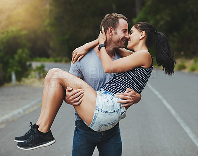 Buy stock photo Shot of a young man romantically carrying his girlfriend down a road outdoors