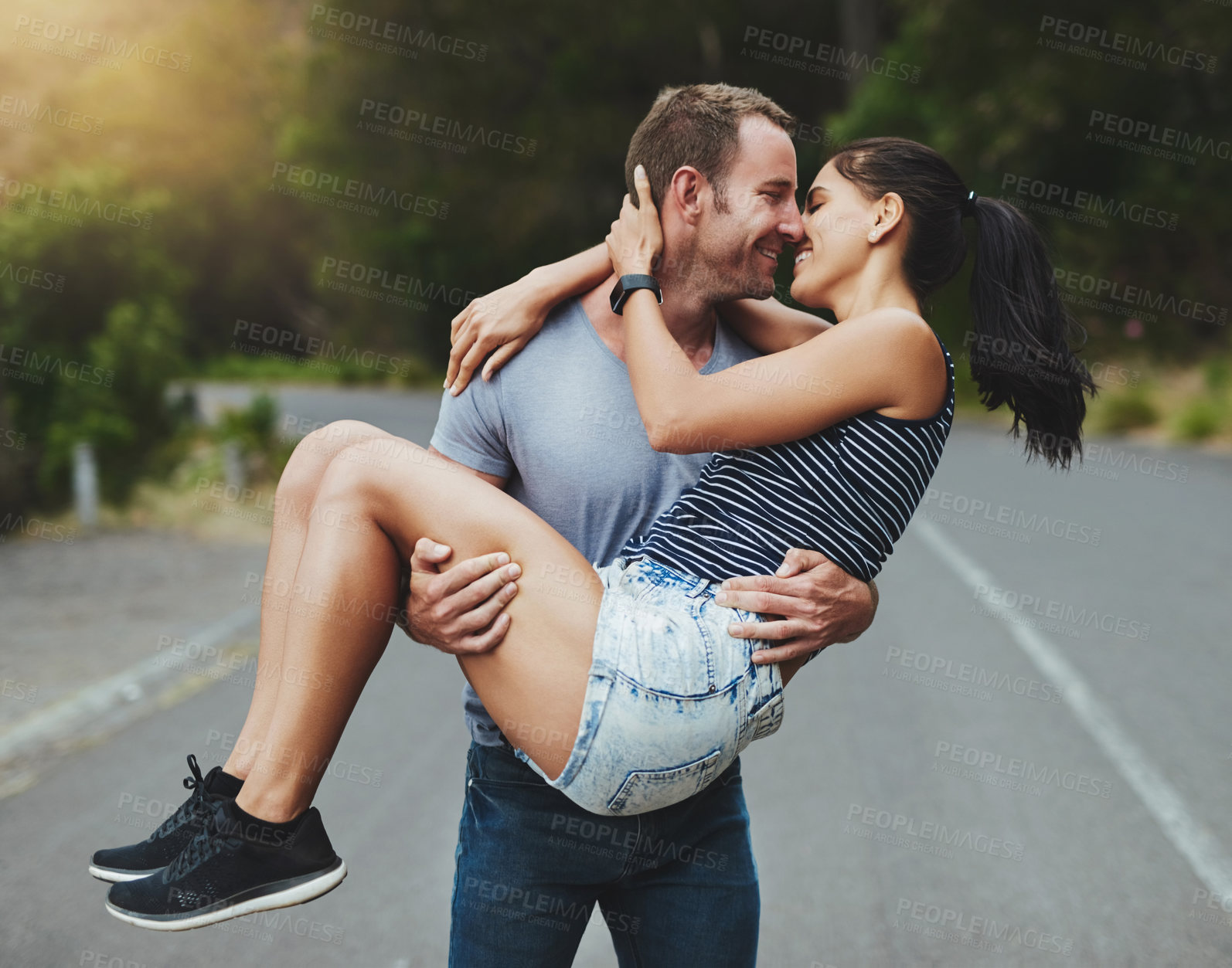 Buy stock photo Shot of a young man romantically carrying his girlfriend down a road outdoors