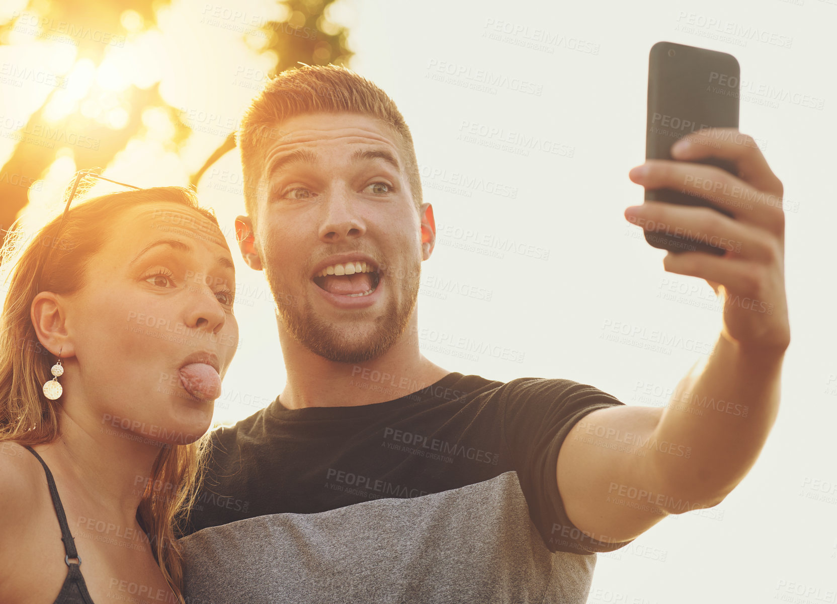 Buy stock photo Shot of a silly young couple posing for a selfie together outside