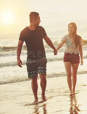Buy stock photo Shot of an affectionate couple walking hand in hand on the beach