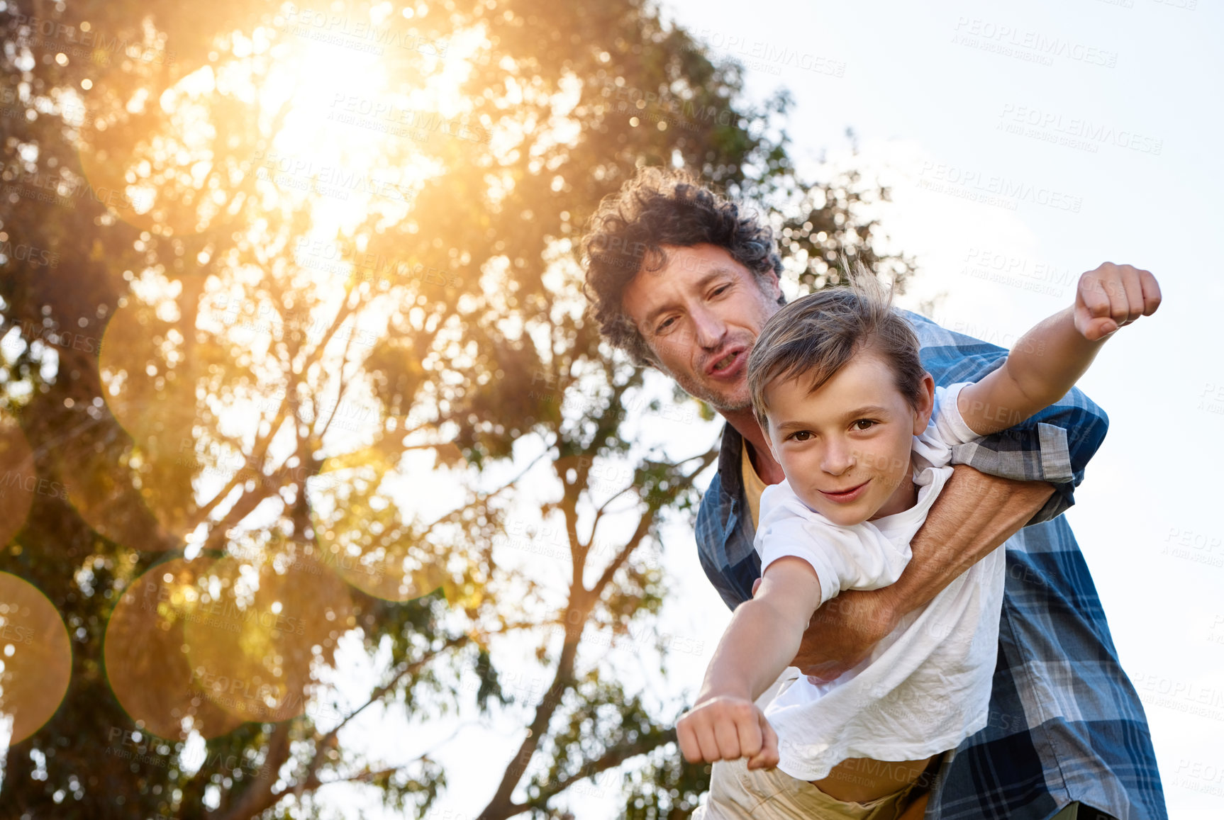 Buy stock photo Father, portrait and son playing plane outdoor with happiness for summer or holiday as family. Man, boy and smile by tree in garden with fun for love, freedom and fun together as superhero flying