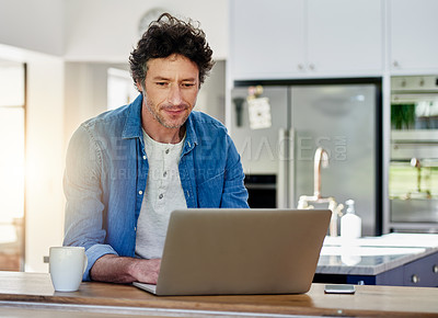 Buy stock photo Shot of a bachelor using his laptop while sitting in the kitchen