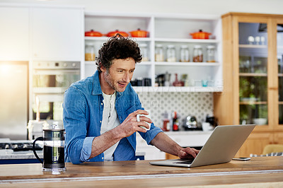 Buy stock photo Shot of a bachelor using his laptop while enjoying a cup of coffee in the kitchen