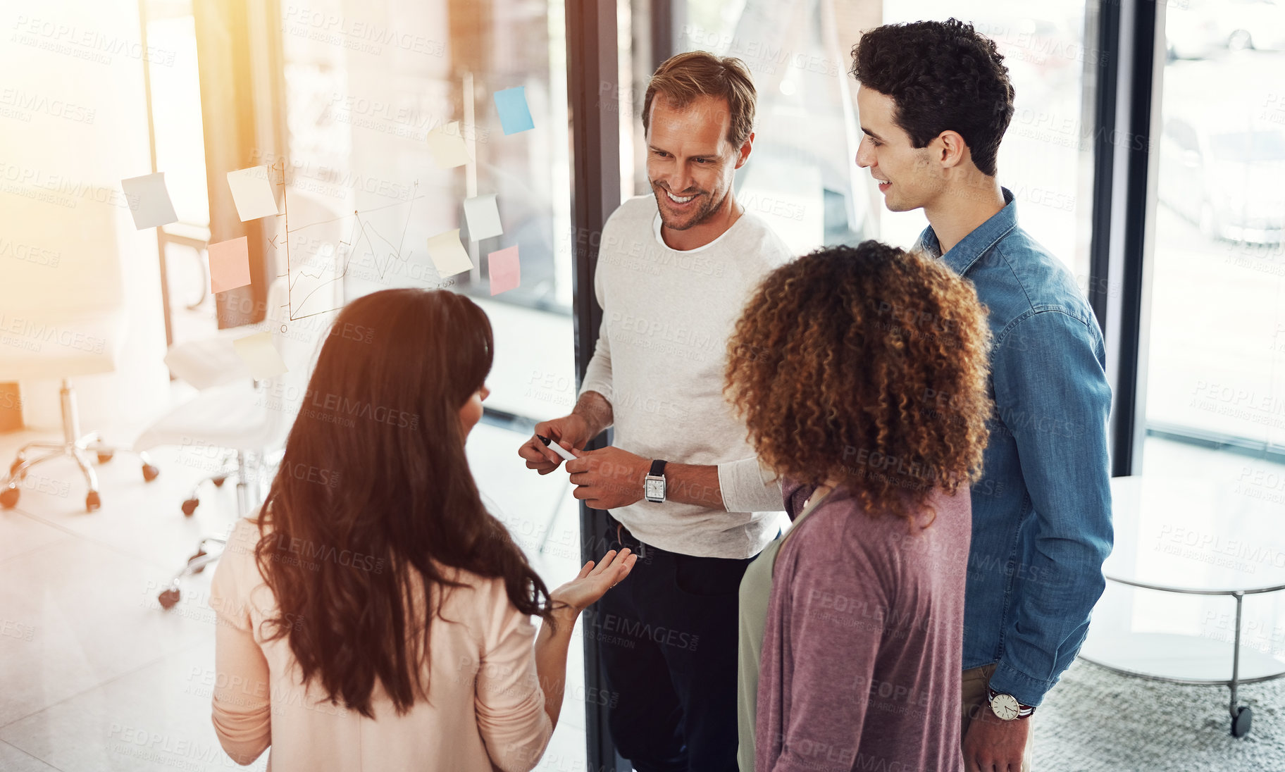 Buy stock photo Cropped shot of a group of young designers brainstorming with notes on a glass wall in an office