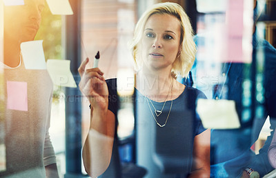 Buy stock photo Cropped shot of a group of young designers brainstorming with notes on a glass wall in an office