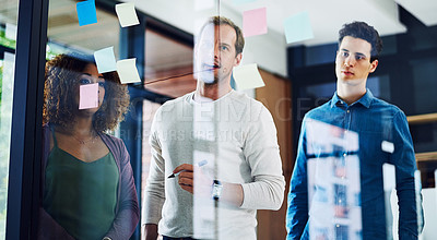 Buy stock photo Cropped shot of a group of young designers brainstorming with notes on a glass wall in an office