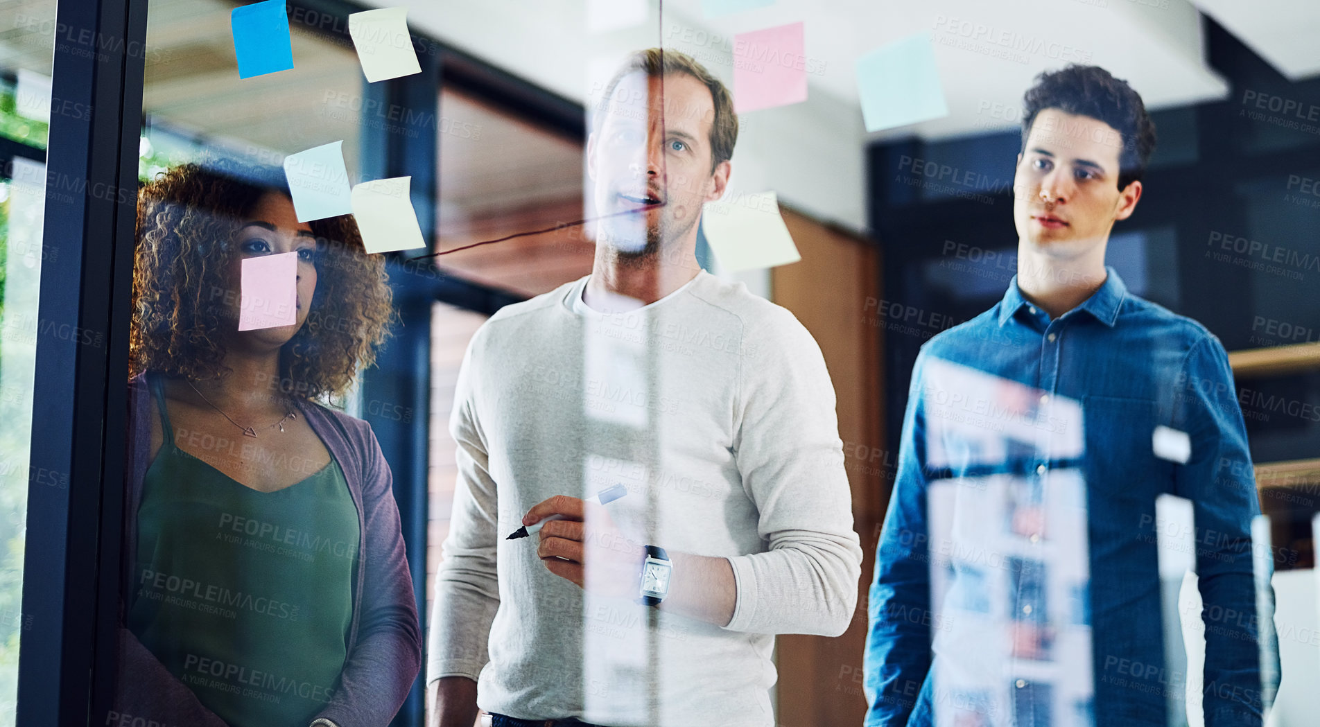 Buy stock photo Cropped shot of a group of young designers brainstorming with notes on a glass wall in an office