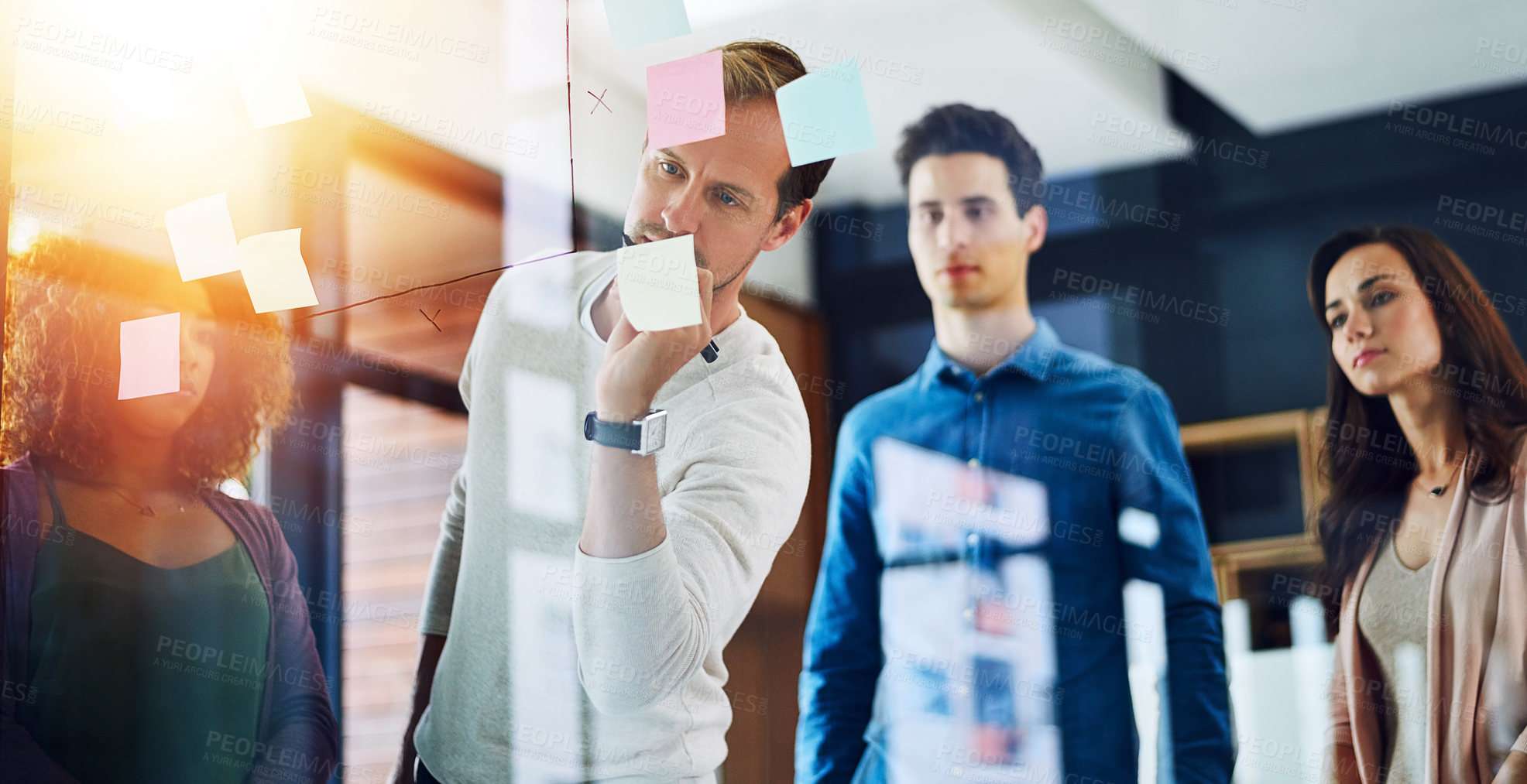 Buy stock photo Cropped shot of a group of young designers brainstorming with notes on a glass wall in an office