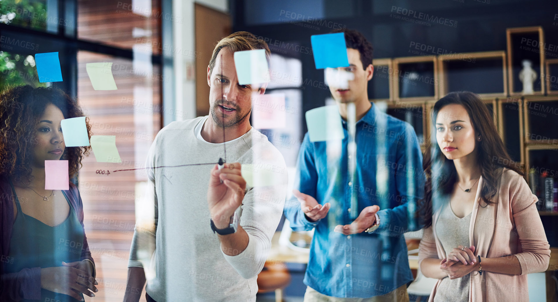 Buy stock photo Cropped shot of a group of young designers brainstorming with notes on a glass wall in an office