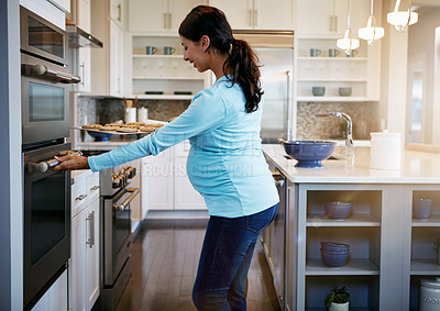 Buy stock photo Cropped shot of a pregnant woman taking a tray of cookies out of the oven