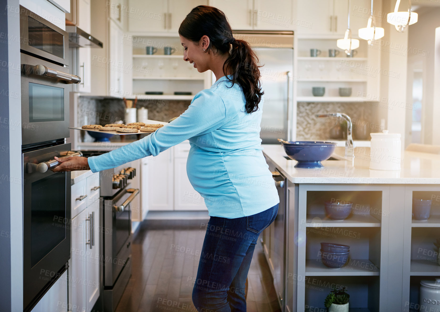 Buy stock photo Cropped shot of a pregnant woman taking a tray of cookies out of the oven